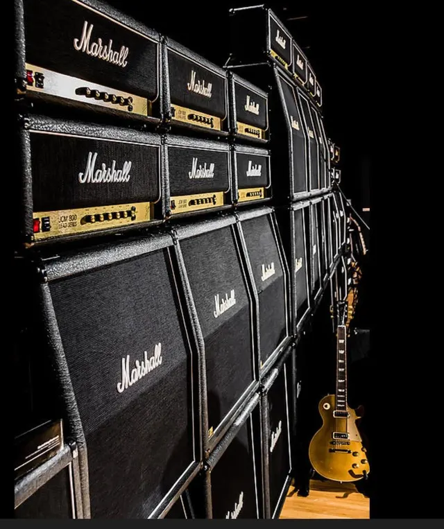 A wall of Marshall stacks with a gold-top Les Paul leaning against it.