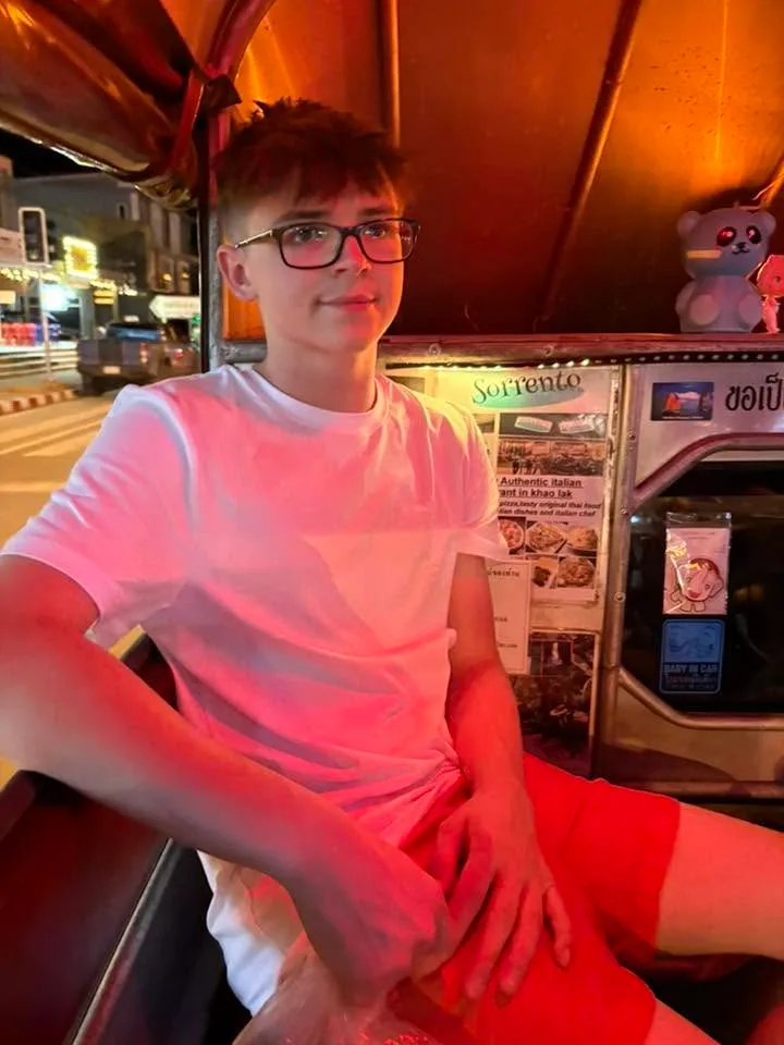 Kyle Endean, smiling, sitting in a tuk-tuk on a street at night while travelling.
